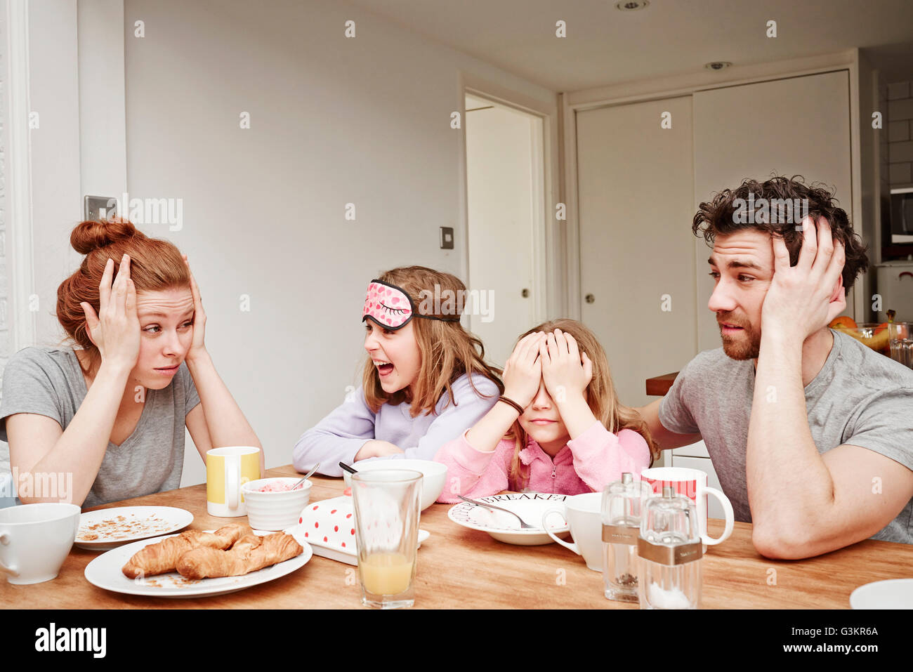Stanco metà adulto genitori al tavolo per la colazione con due figlie Foto Stock