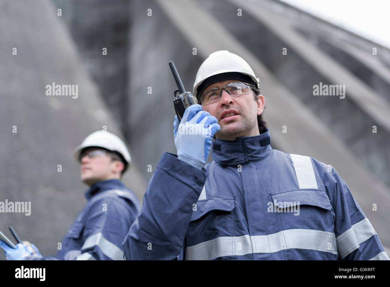 Lavoratore utilizzando walkie talkie al piede della diga a centrale idroelettrica Foto Stock