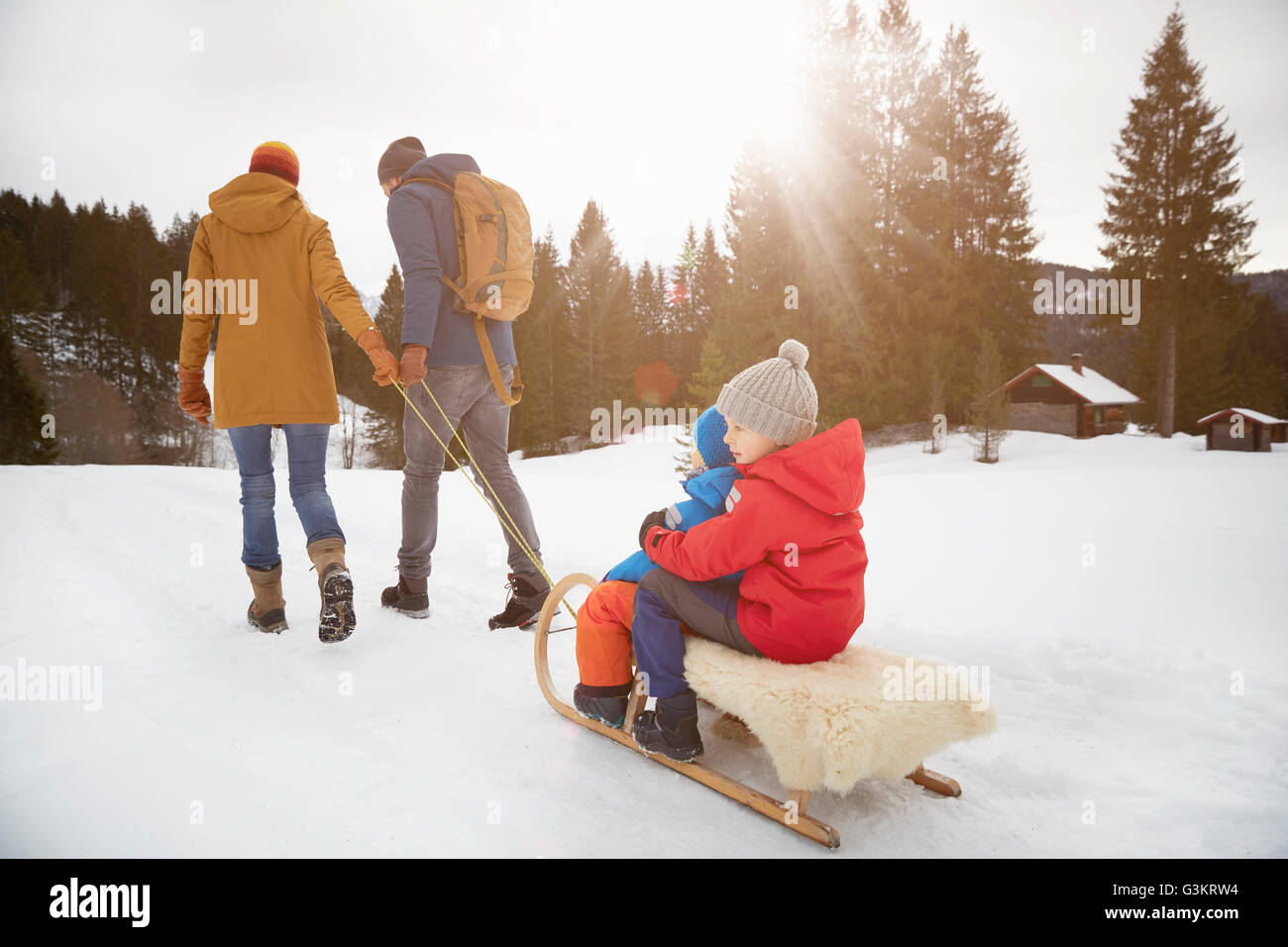 Vista posteriore dei genitori tirando figli sul toboga in snow landscape, Elmau, Baviera, Germania Foto Stock