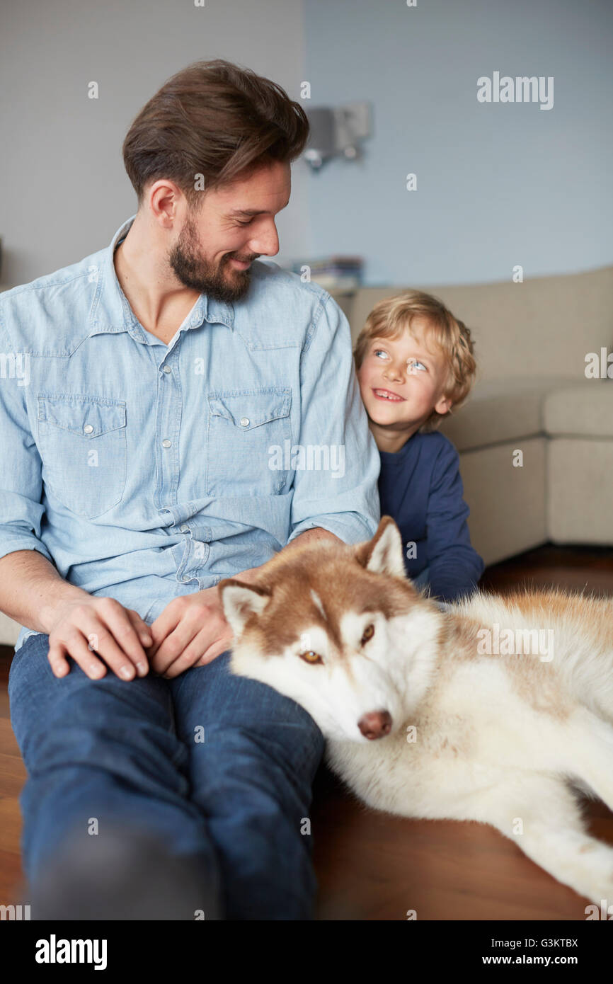Padre e figlio seduti con il cane faccia a faccia sorridente Foto Stock
