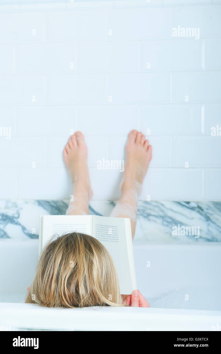 Vista posteriore della bionda ragazza dai capelli leggendo un libro nella vasca da bagno con piedini fino Foto Stock
