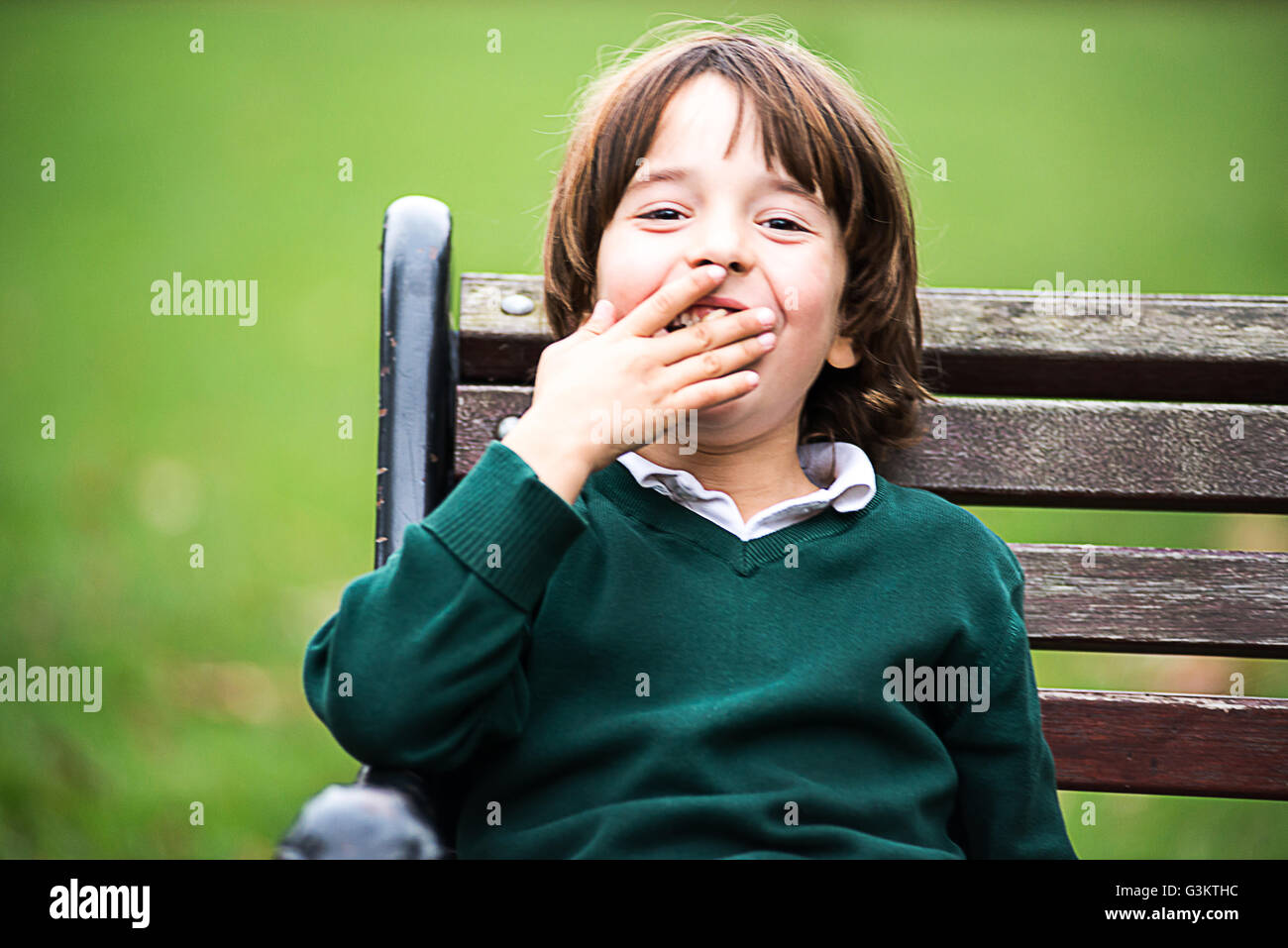Ragazzo su una panchina nel parco, la mano sulla bocca guardando sorridente della fotocamera Foto Stock