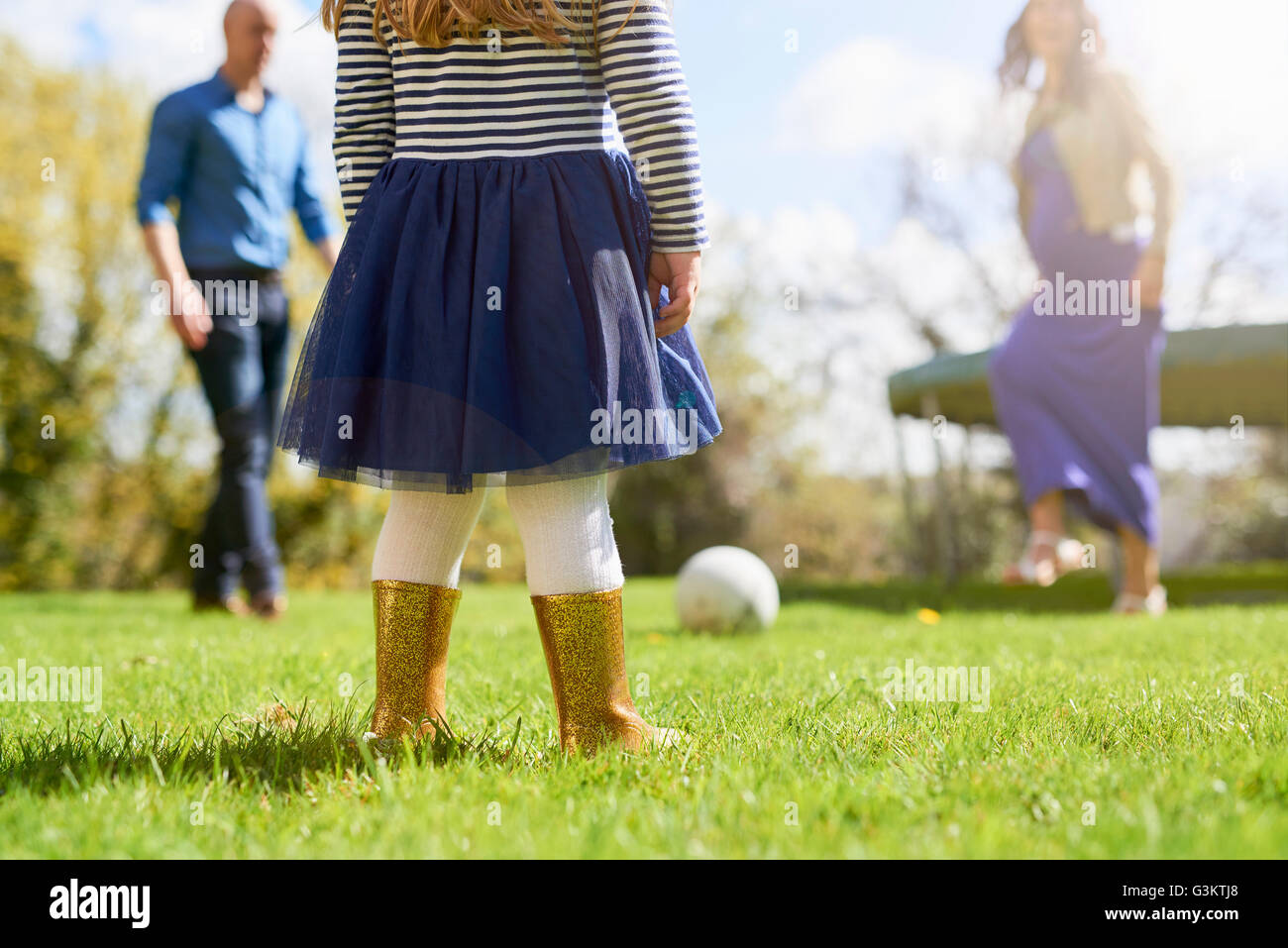 Sezione bassa della ragazza nel giardino con la famiglia a giocare con il calcio Foto Stock