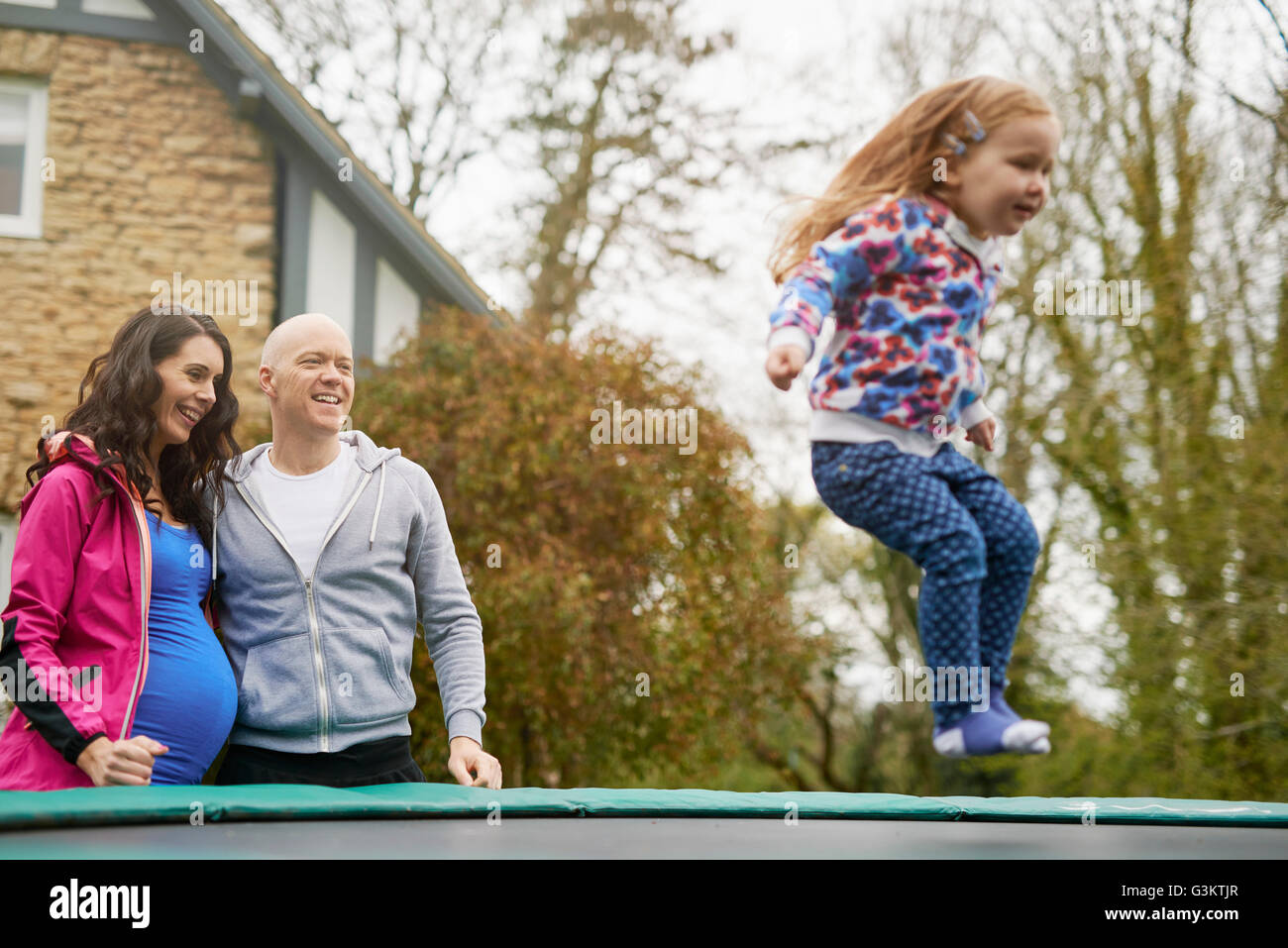 I genitori a guardare la figlia rimbalzare sul trampolino Foto Stock