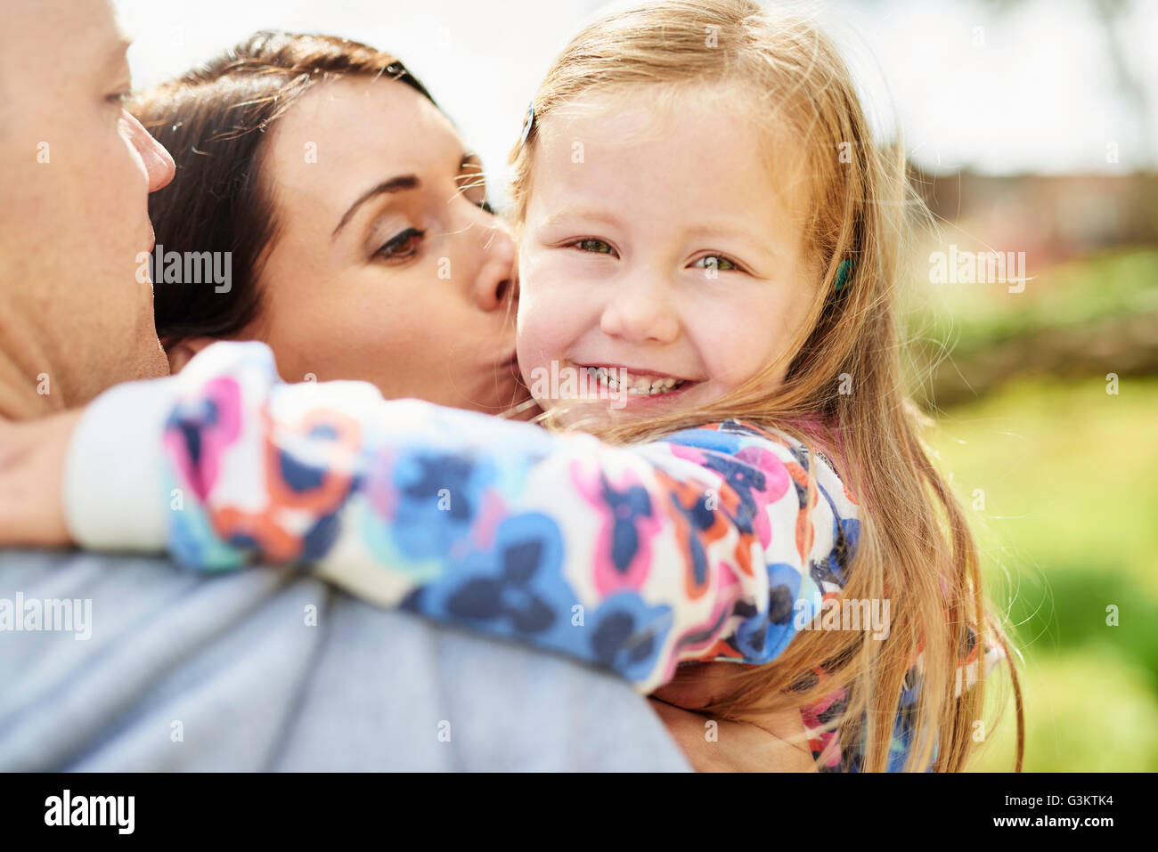 Sulla spalla vista della madre baciare sorridente figlia sulla guancia Foto Stock