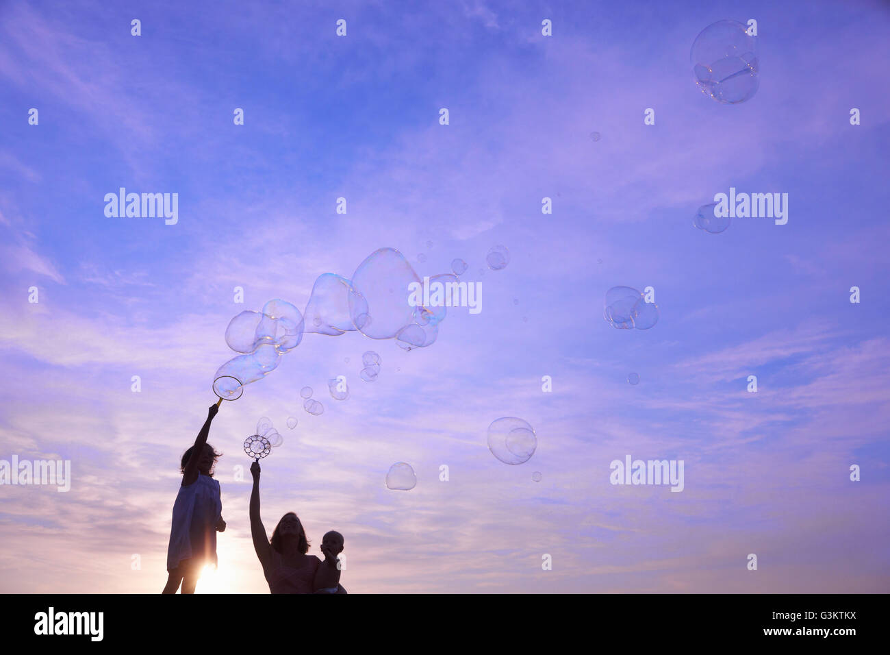 Stagliano Donna con bambino figlio e figlia soffiare bolle contro il cielo blu, Buonconvento, Toscana, Italia Foto Stock