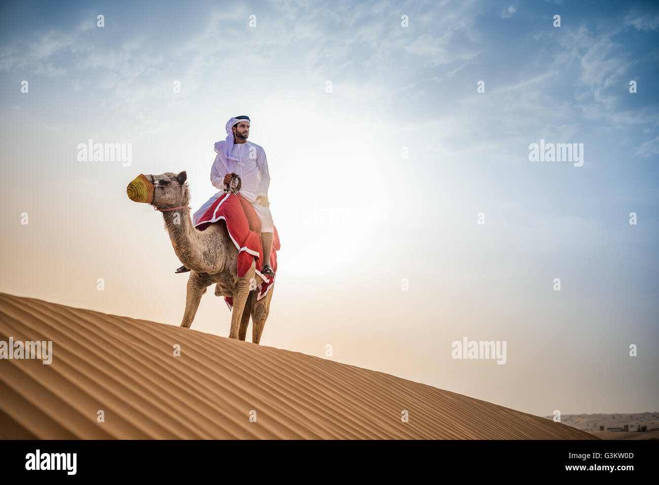 L'uomo indossando il tradizionale del medio oriente a cavallo vestiti cammello nel deserto, Dubai, Emirati Arabi Uniti Foto Stock