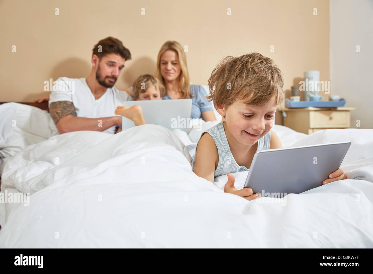 Il padre e la madre a letto con figli utilizzando la tecnologia Foto Stock