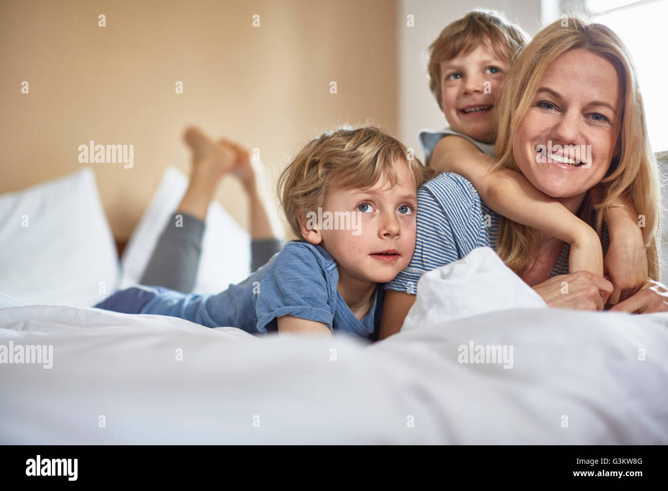 Ragazzi sul letto giacente sulla parte superiore della madre guardando sorridente della fotocamera Foto Stock