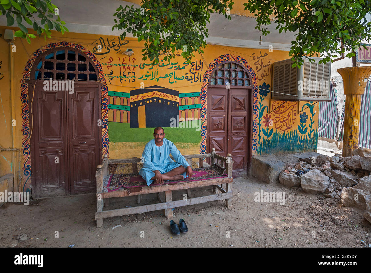 L'uomo, egiziano, seduto davanti alla sua casa dipinta, Valle dei Re, Luxor, Egitto Foto Stock