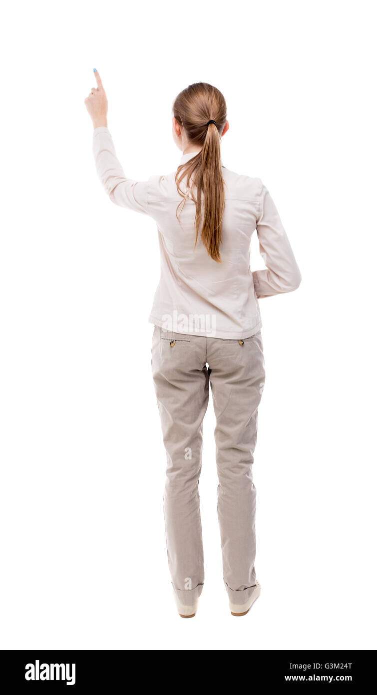 Vista posteriore della donna di puntamento. bella ragazza. Vista posteriore di raccolta persone. vista posteriore di persona. Isolato su sfondo bianco. Una ragazza in piedi in una luce denim tuta e mostra con la sua mano sinistra. Foto Stock