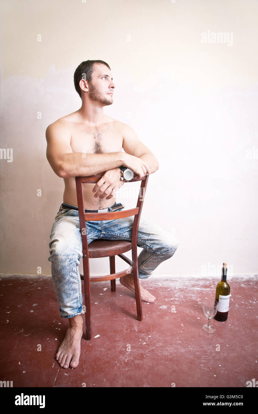 Uomo con una bottiglia di vino seduti su una sedia Foto Stock