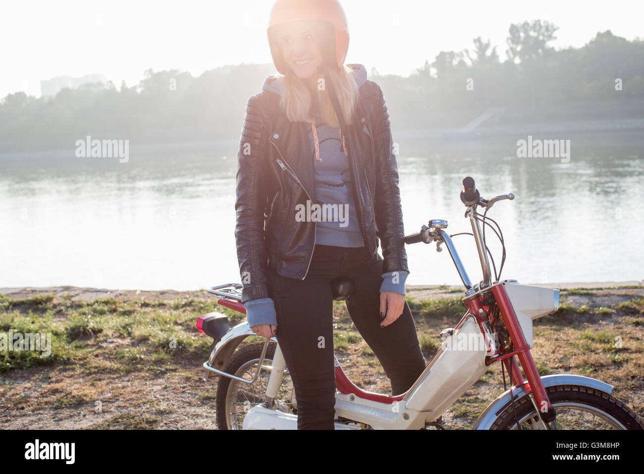 Giovane donna seduta sul ciclomotore retrò, accanto al lago Foto Stock