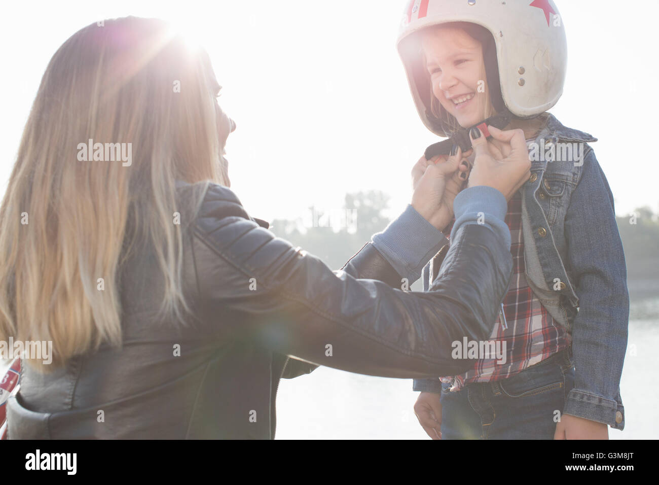 Giovane donna mettendo casco su figlia, sorridente Foto Stock