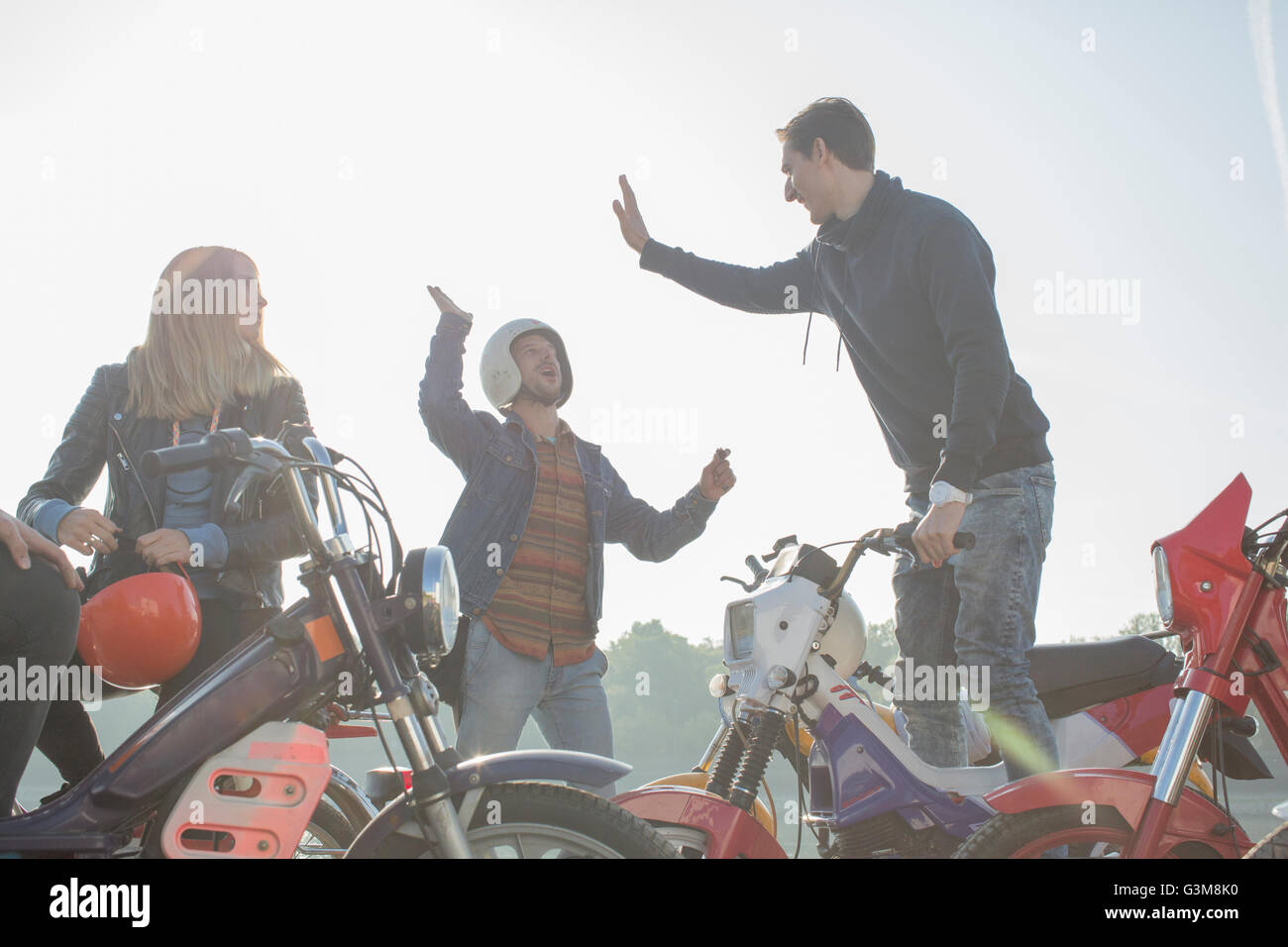 Gruppo di amici seduti sui ciclomotori, due uomini dando alta cinque Foto Stock