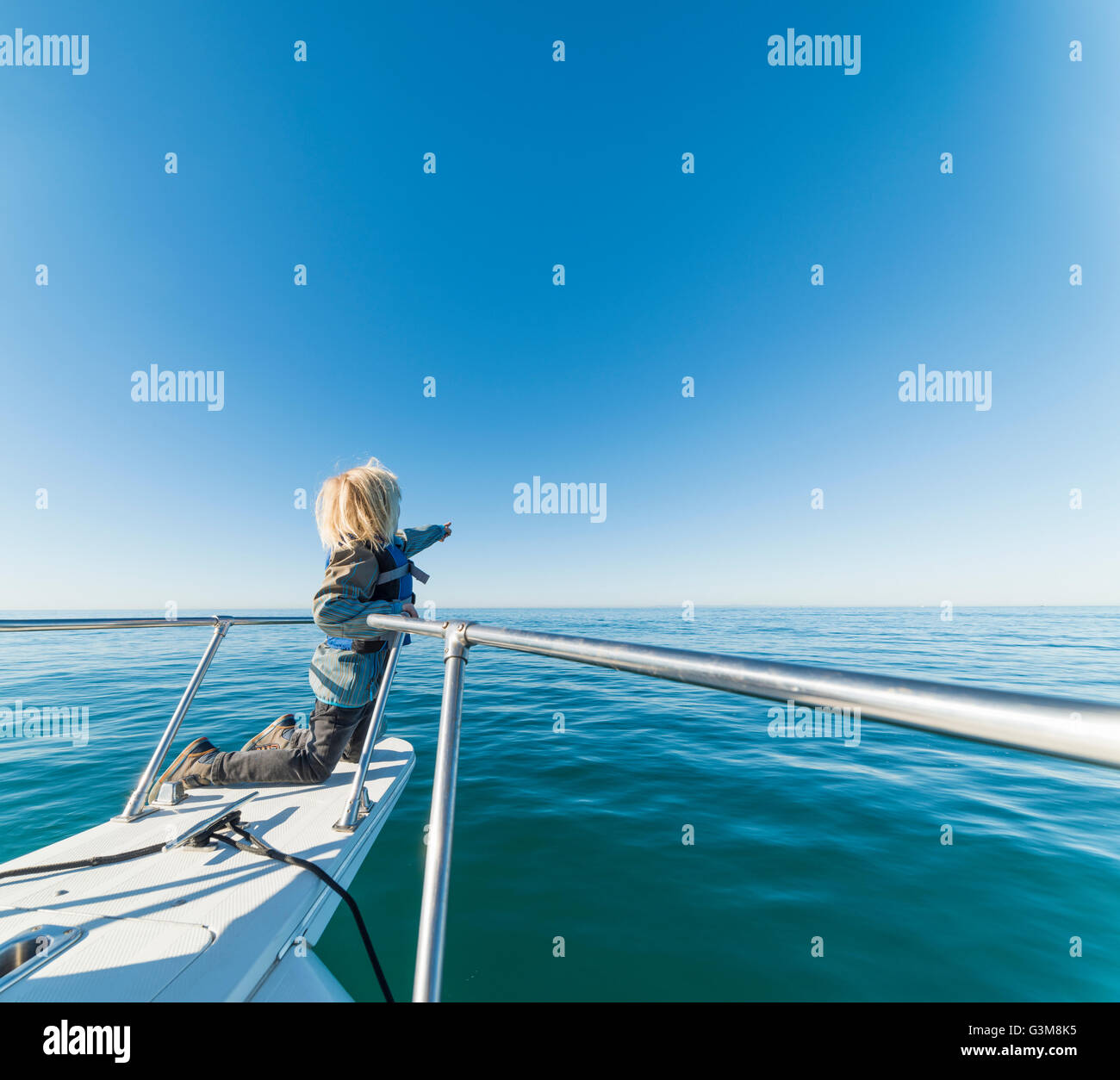 Ragazzo inginocchiato a bordo di navi di prua di una barca a vela che guarda lontano puntando Foto Stock