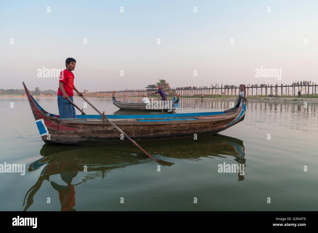 Adulto Uomo birmano in una barca sul lago Taungthaman, Amarapura, Myanmar. In fondo è U Bein legno teak bridge. Foto Stock