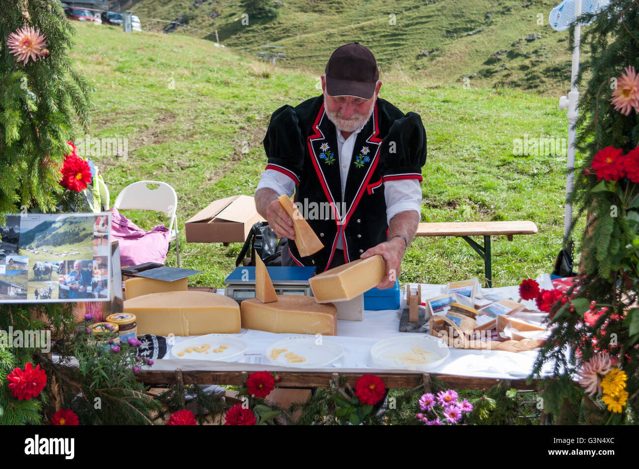 Swiss uomo in Bernese abito folcloristico disponendo il formaggio per la vendita su un mercato. Mägisalp, Hasliberg e Svizzera. Foto Stock