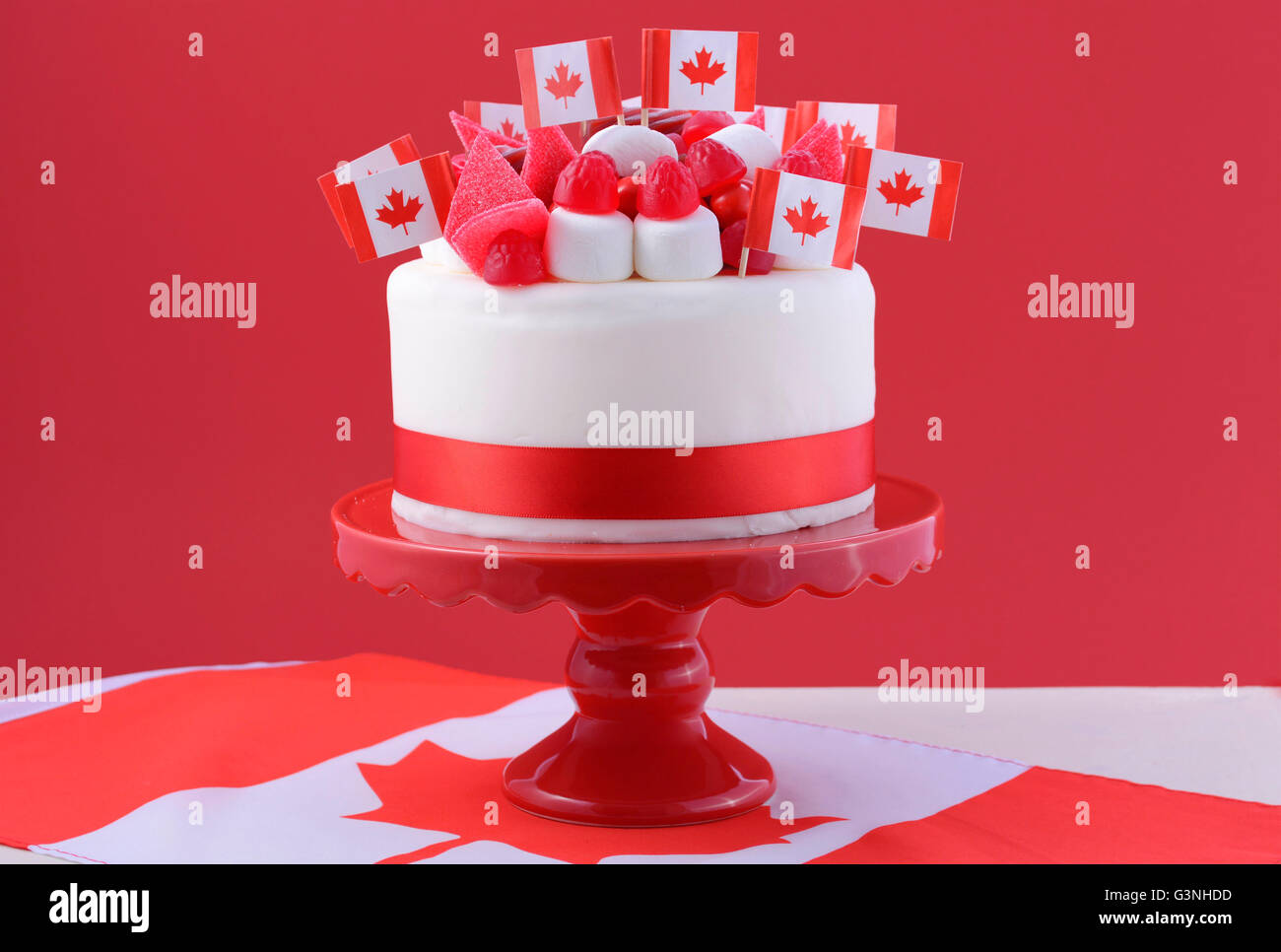 Happy Canada Day celebrazione torta con bandiere, marshmallow e caramelle decorazioni su una torta rosso stand su un tavolo bianco contro un r Foto Stock