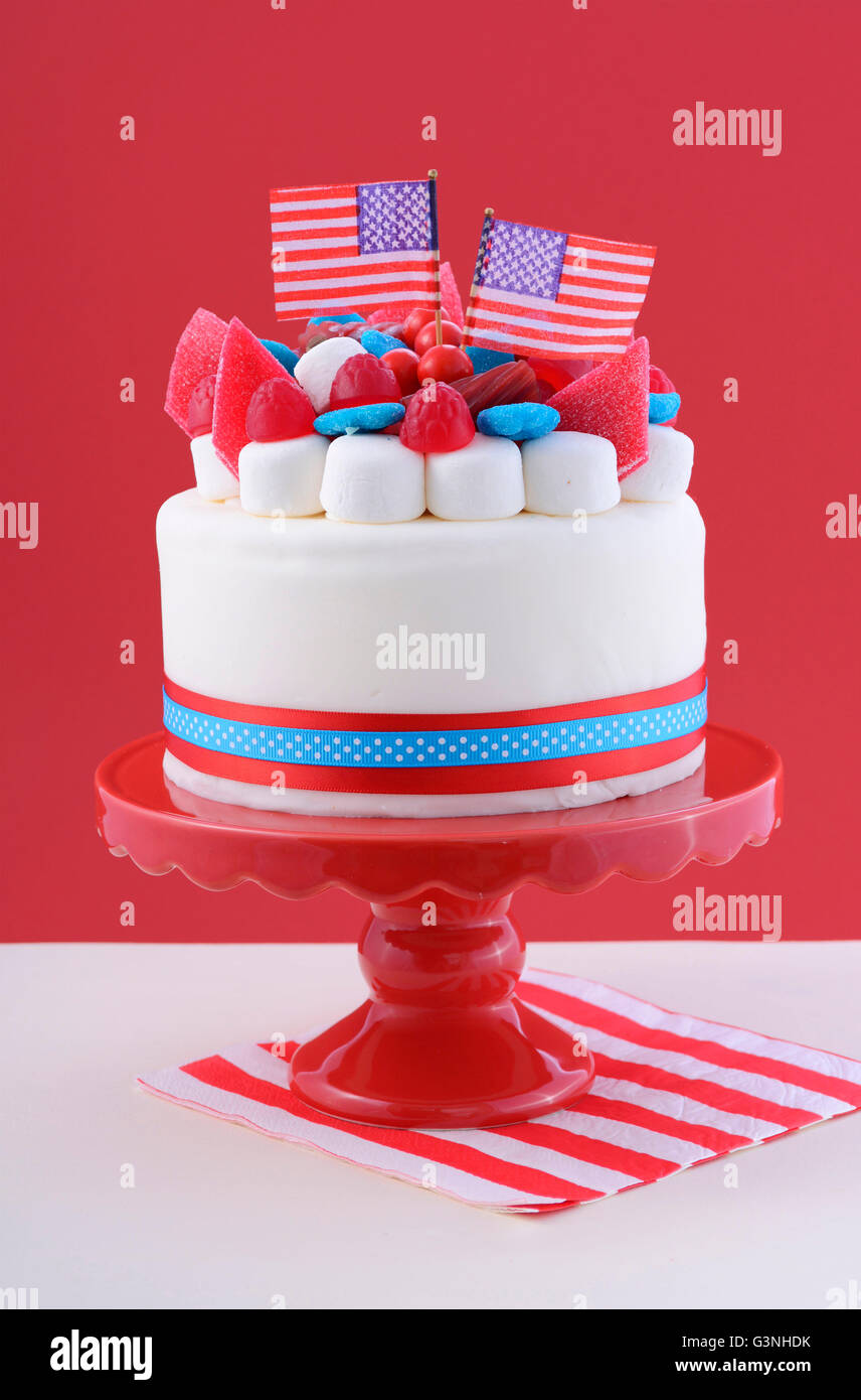 Felice Quarta di luglio celebrazione torta con bandiere, marshmallow e caramelle decorazioni su una torta rosso stand su un tavolo bianco contro Foto Stock