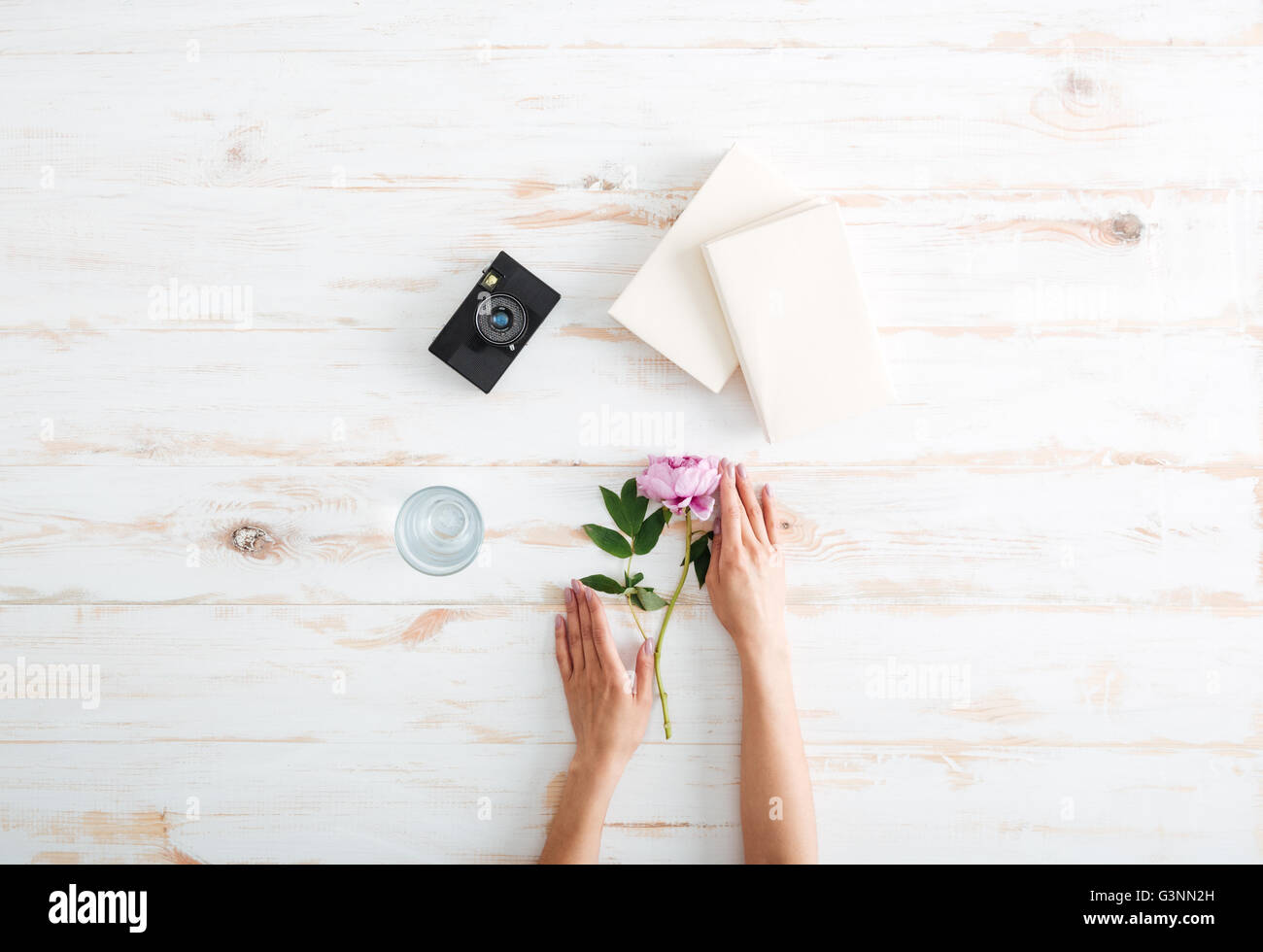 Le donne le mani con la peonia fiore, libri, una videocamera e un bicchiere di acqua sulla scrivania in legno Foto Stock