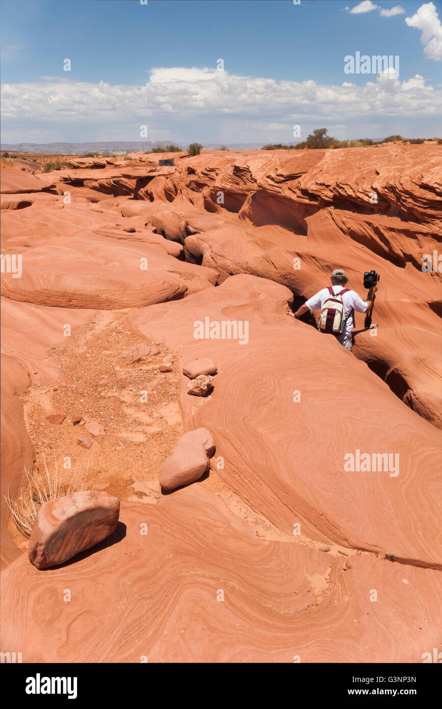 L'uomo discende in una stretta fessura in colorate di rosso il paesaggio di roccia nel sud-ovest americano slot canyon su un giorno di estate Foto Stock