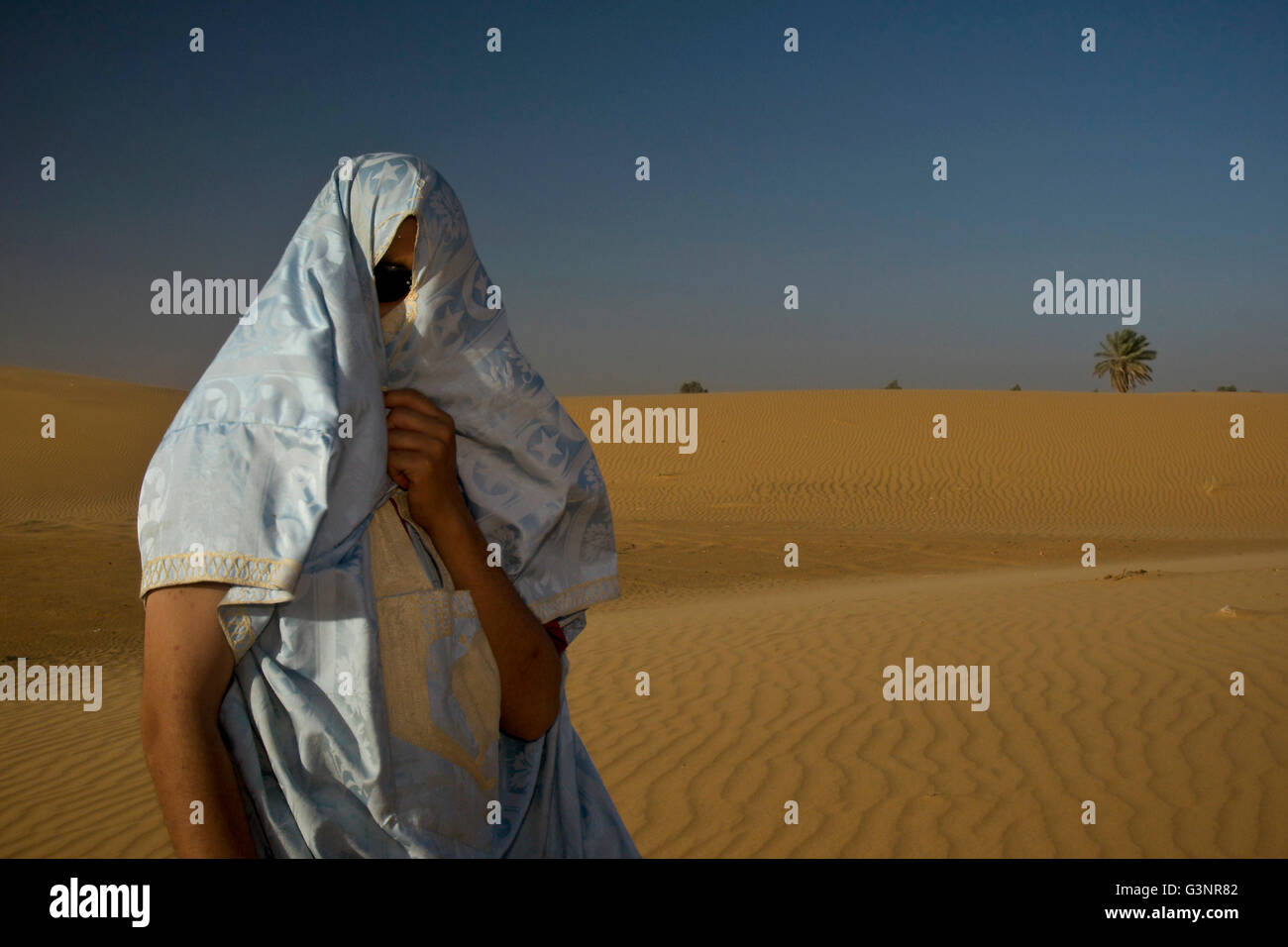 Un uomo locale sorge su una duna di sabbia di seta blu e oro tessuto avvolto intorno alla sua testa e viso per proteggere lui dal soffiaggio s Foto Stock