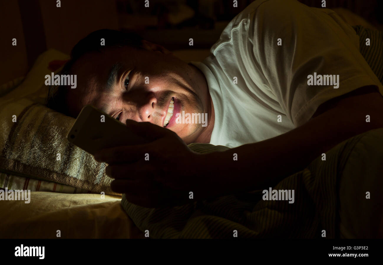 Un uomo per la messaggistica di testo durante la notte su un letto Foto Stock