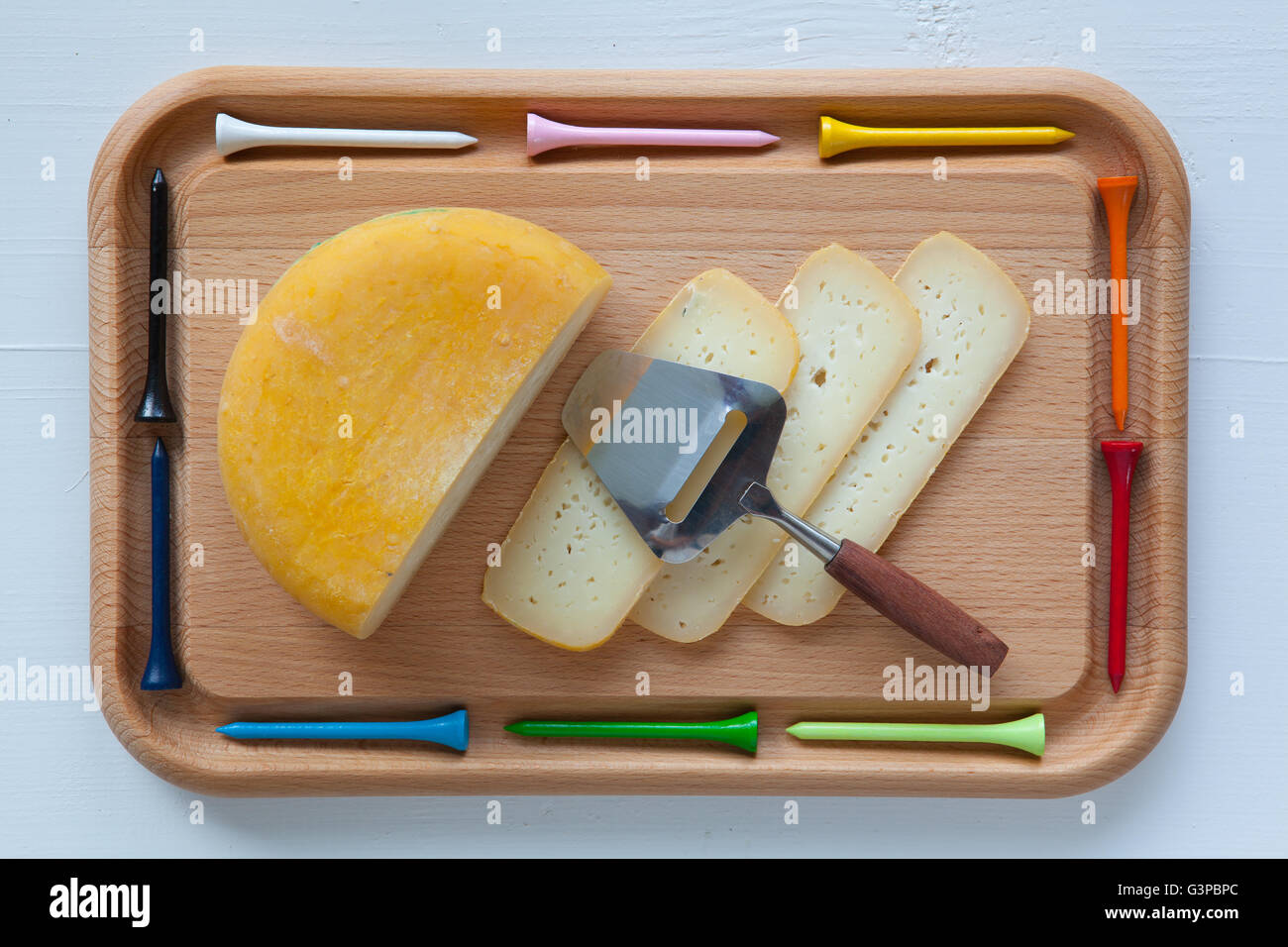 Blocco di gustosi formaggi sul tagliere con un coltello e golf tees, isolato su bianco scrivania in legno Foto Stock