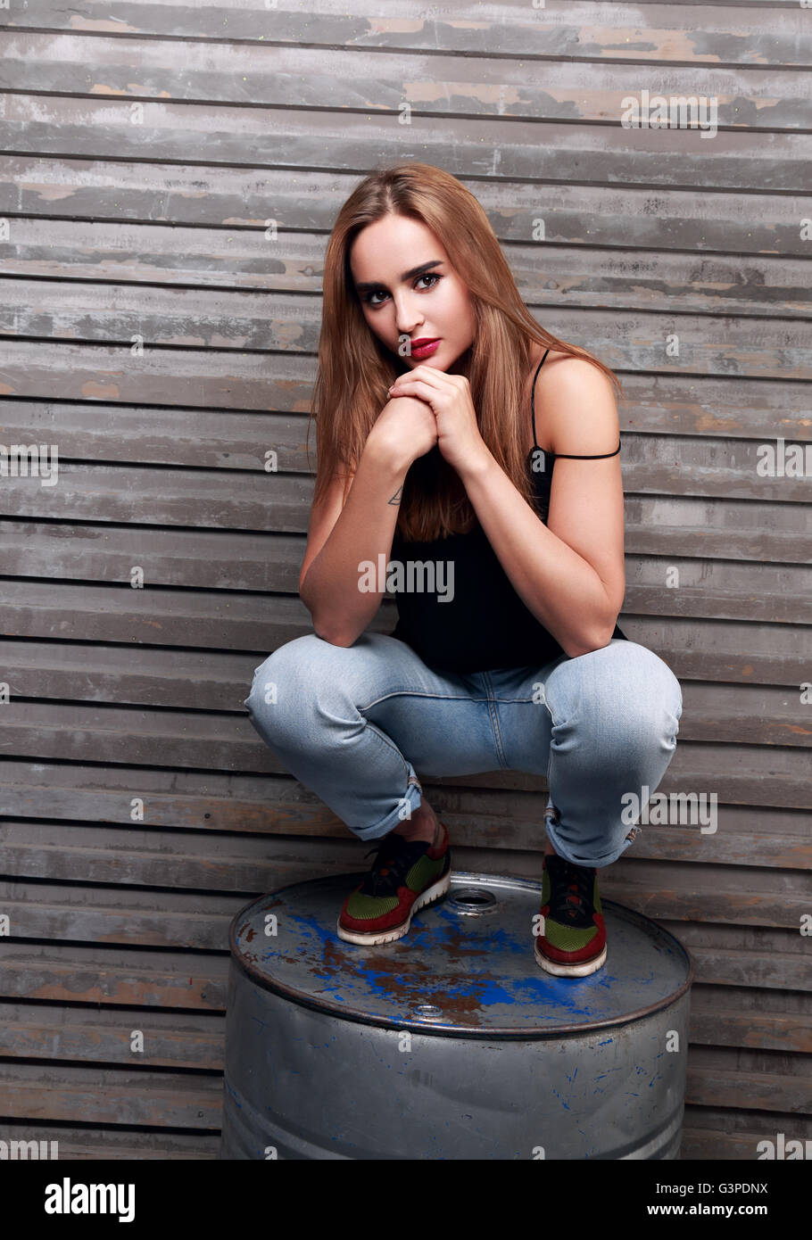 Bellissimi capelli lunghi donna pensare con le mani al di sotto di volto seduto sulla botte di ferro sul muro di sfondo Foto Stock