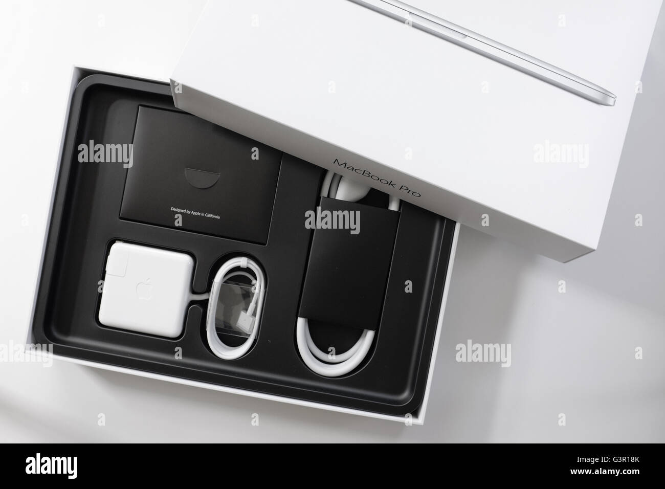 MacBook Pro i cavi nella loro confezione originale fotografati contro uno sfondo bianco. Foto Stock