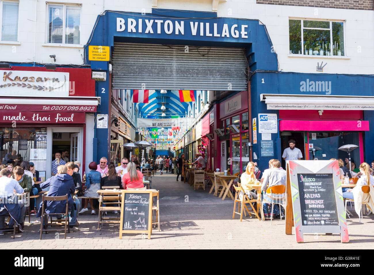 Persone mangiare fuori l'ingresso principale della Brixton Village market, una comunità multiculturale con mercato negozi indipendenti Foto Stock