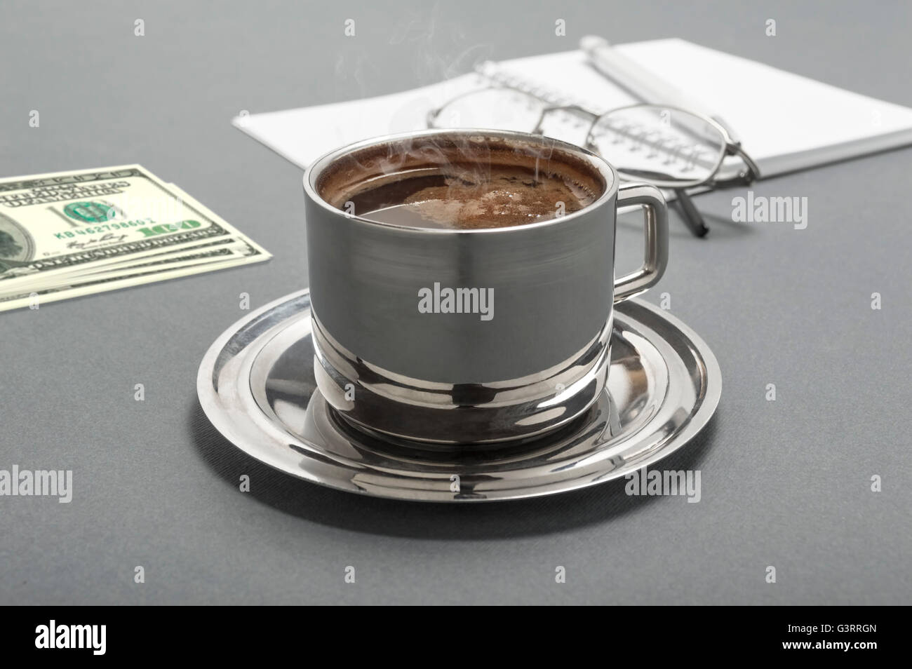 Still Life foto con tazza di caffè, prenota, penna, denaro e occhiali su sfondo grigio. Il fuoco selettivo sulla tazza di caffè. Foto Stock