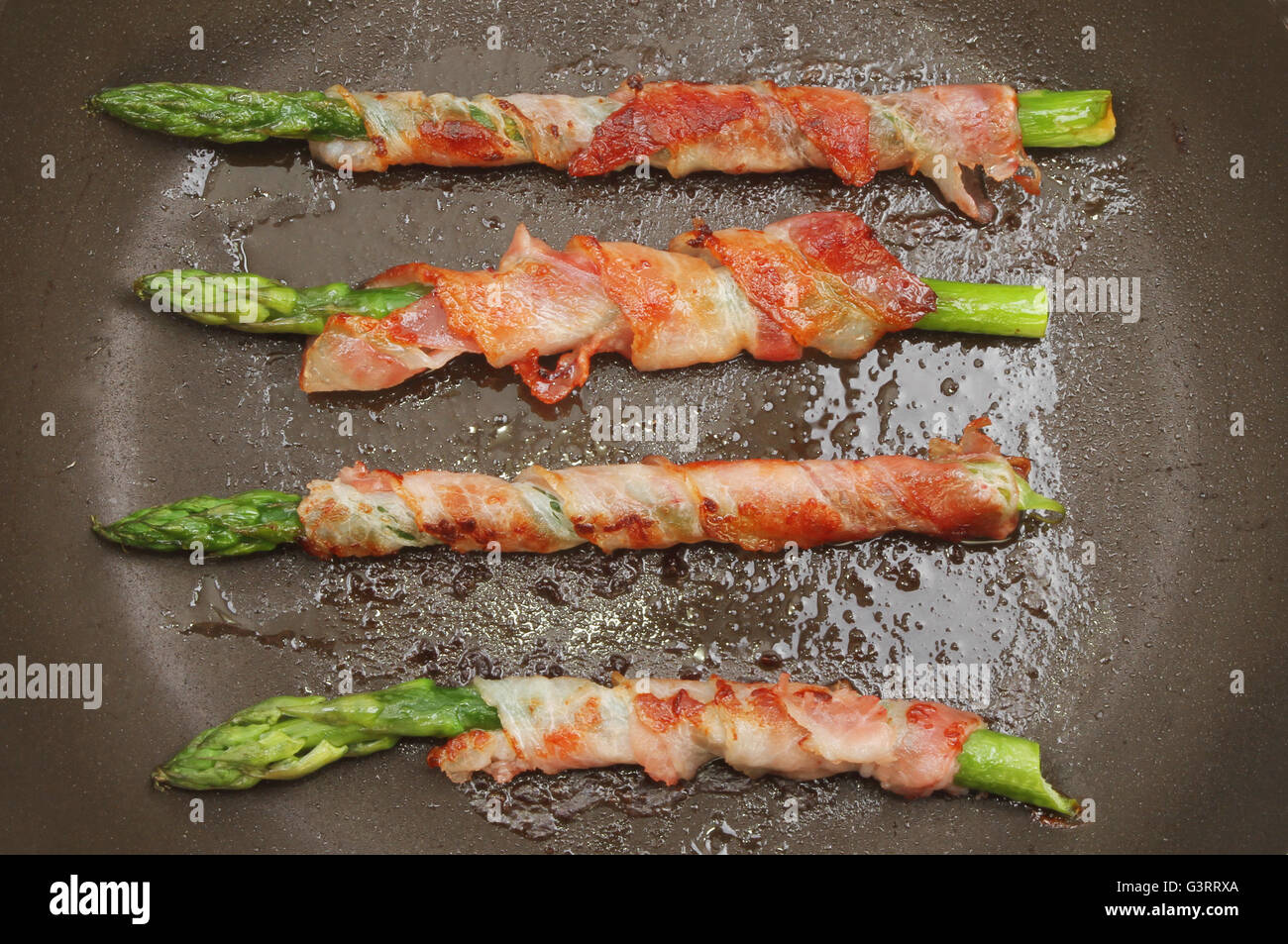 Pancetta asparagi avvolto una cottura in padella Foto Stock