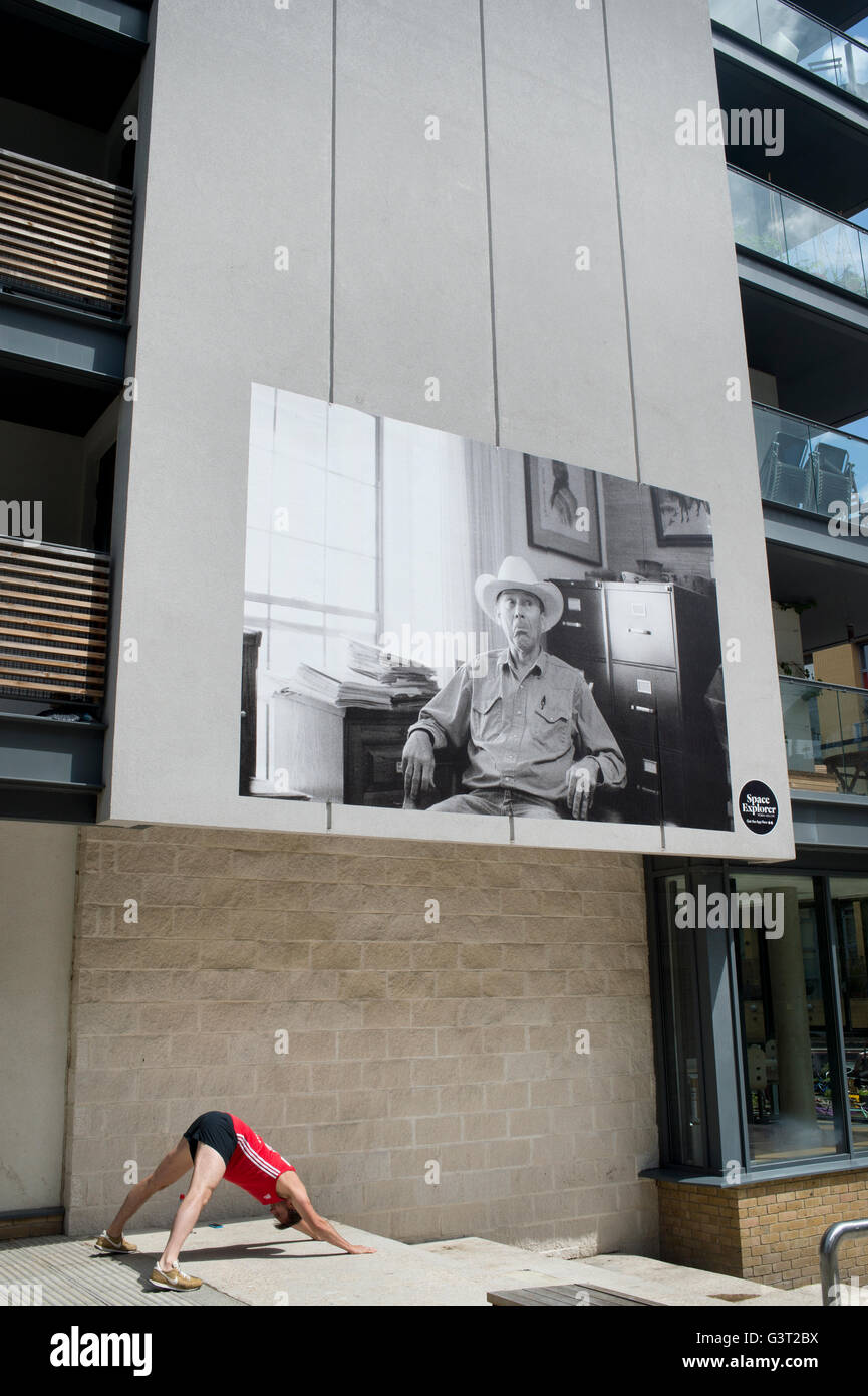 Un uomo fa un po' di yoga pone sotto una foto di grandi dimensioni, parte di una fiera locale Foto Stock