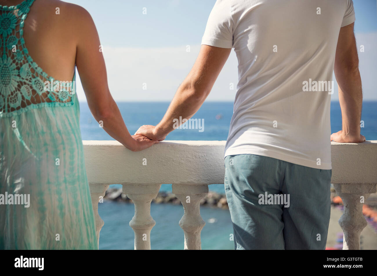 L'Italia, le Cinque Terre, Monterosso, matura in piedi sul balcone con vista sul mare e tenendo le mani Foto Stock