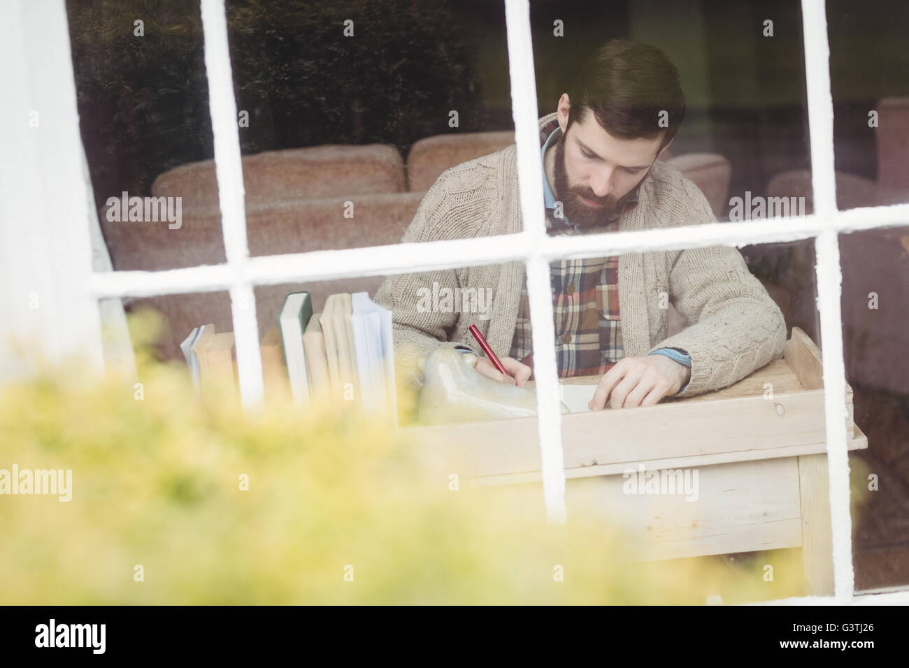 Attraente hipster uomo iscritto alla scrivania davanti alla finestra Foto Stock