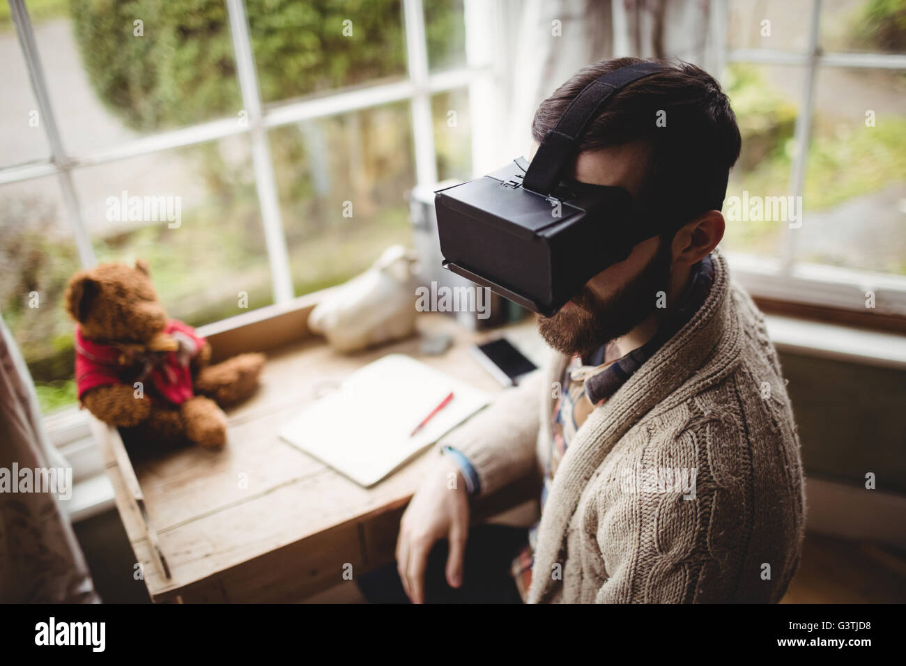 Hipster uomo utilizzando smart bicchieri mentre posti a sedere alla scrivania Foto Stock