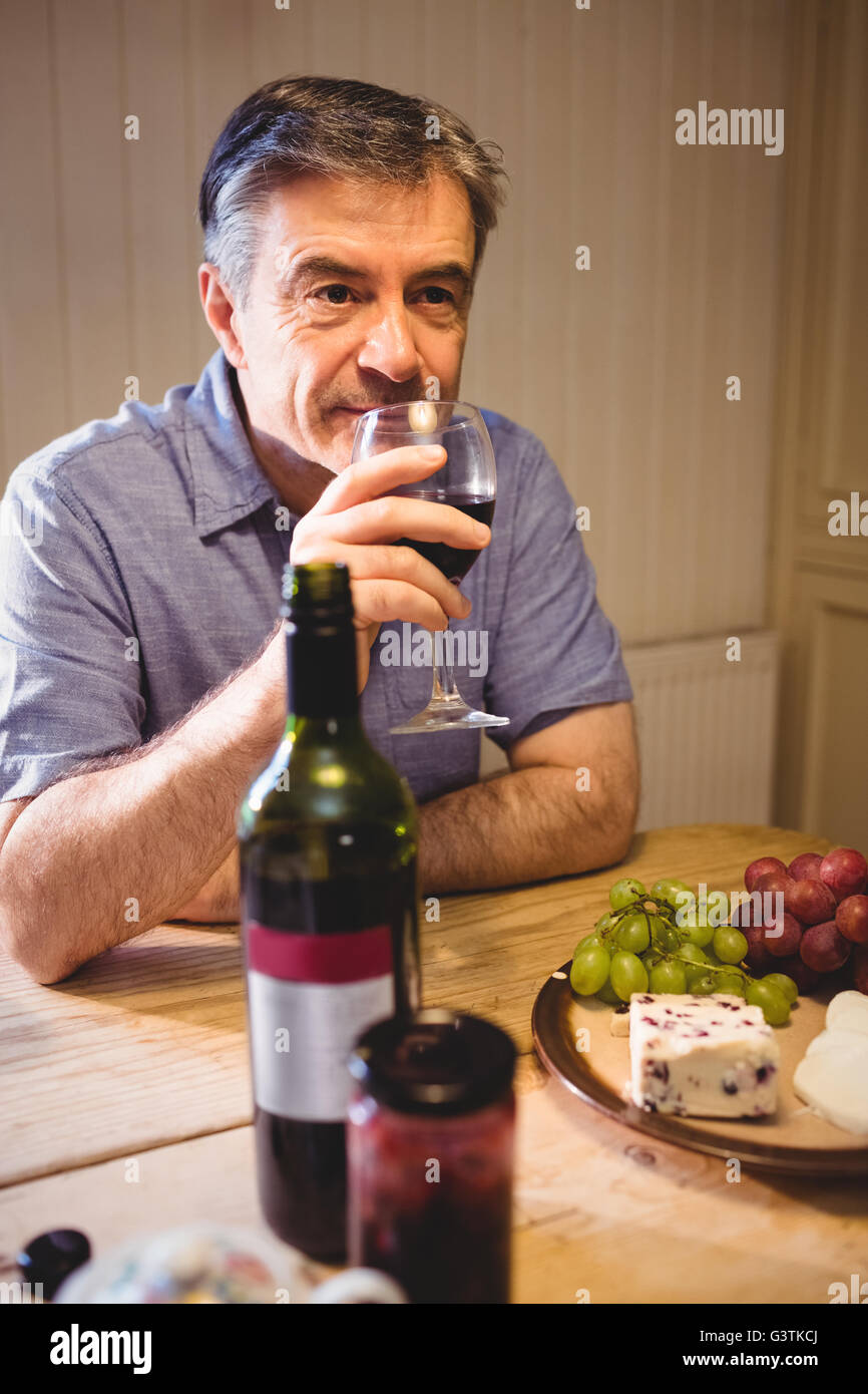 Uomo maturo seduta a tavola e degustazione di vino rosso Foto Stock