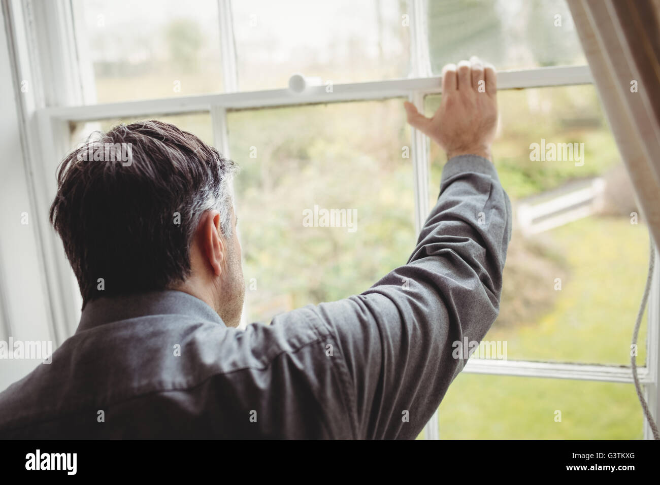 Vista posteriore di uomo maturo guardando attraverso la finestra Foto Stock