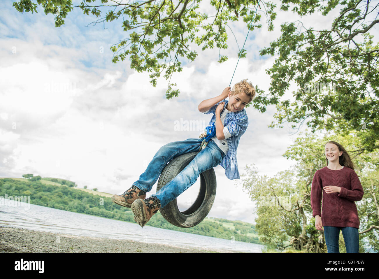 Una ragazza e un ragazzo giocando su un pneumatico appeso a un albero sulla riva accanto a Bala Lake in Galles. Foto Stock