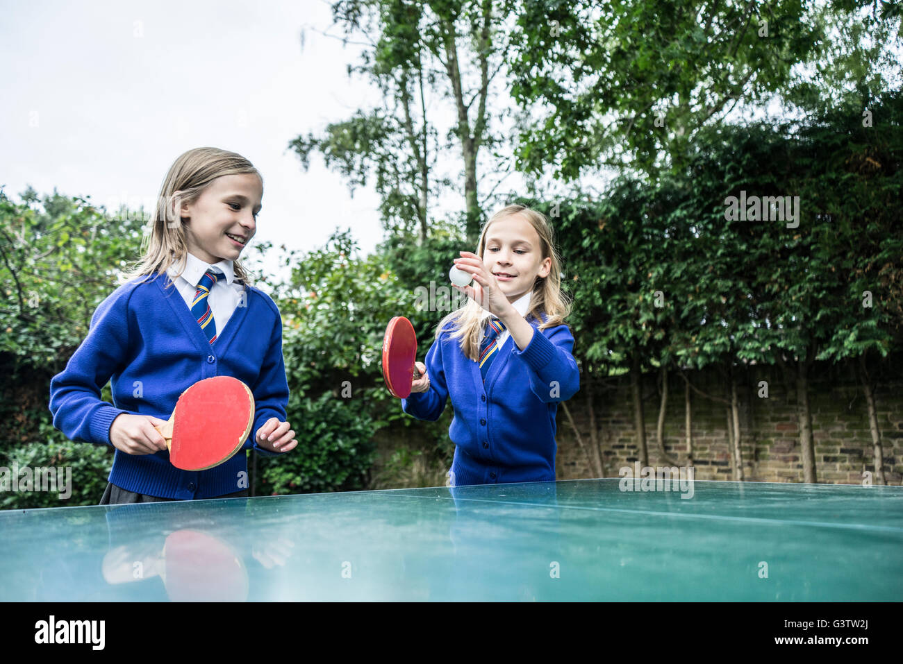 Twin ragazze in uniforme scolastica giocando a ping-pong all'esterno. Foto Stock