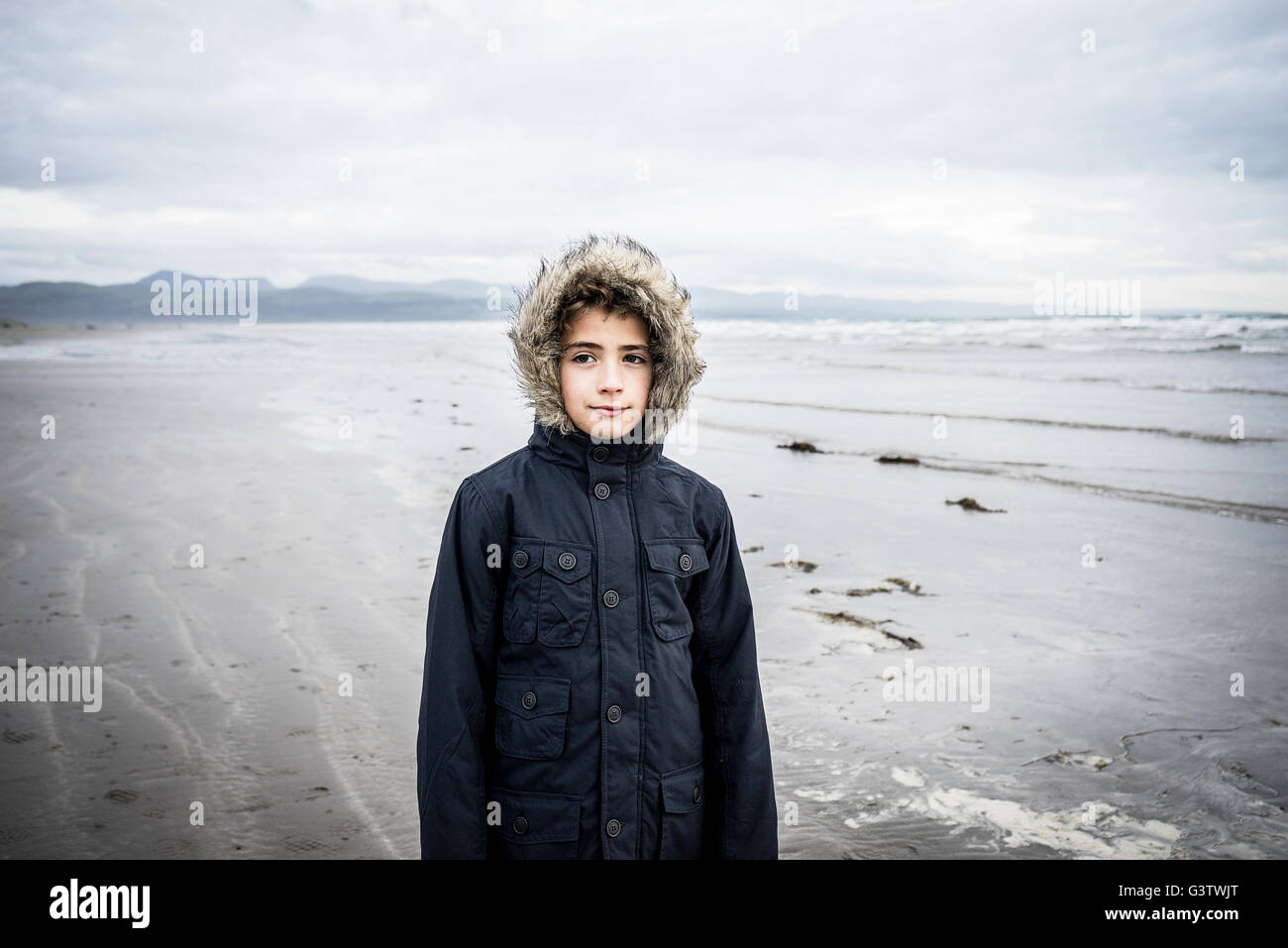 Un giovane ragazzo che sta sulla spiaggia di Porthmadog. Foto Stock