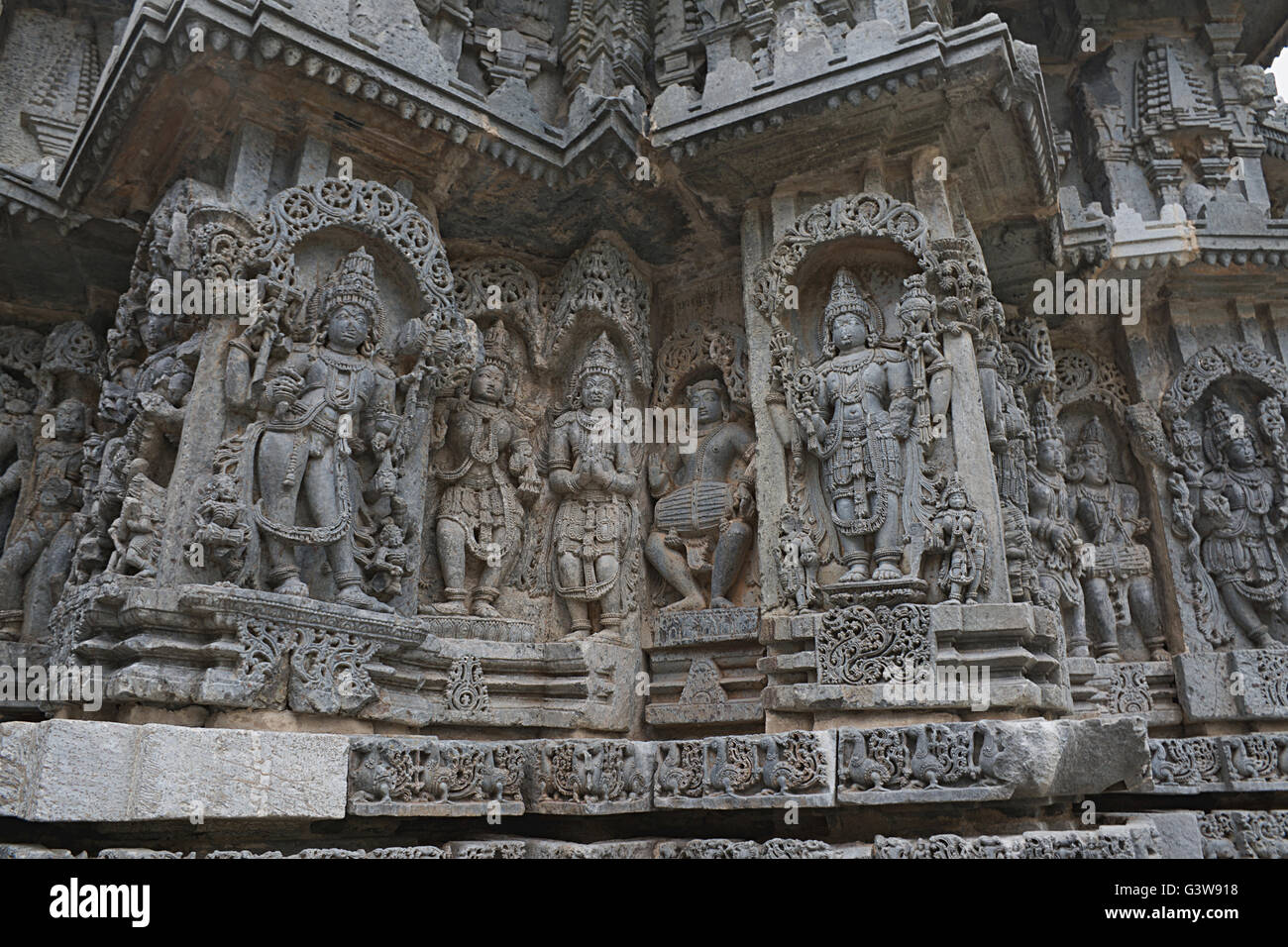 Ornati pannello parete bassorilievi raffiguranti (da sinistra) Bhairava, altre divinità, un drumer, Vishnu Kedareshwara tempio, Halebidu, India Foto Stock