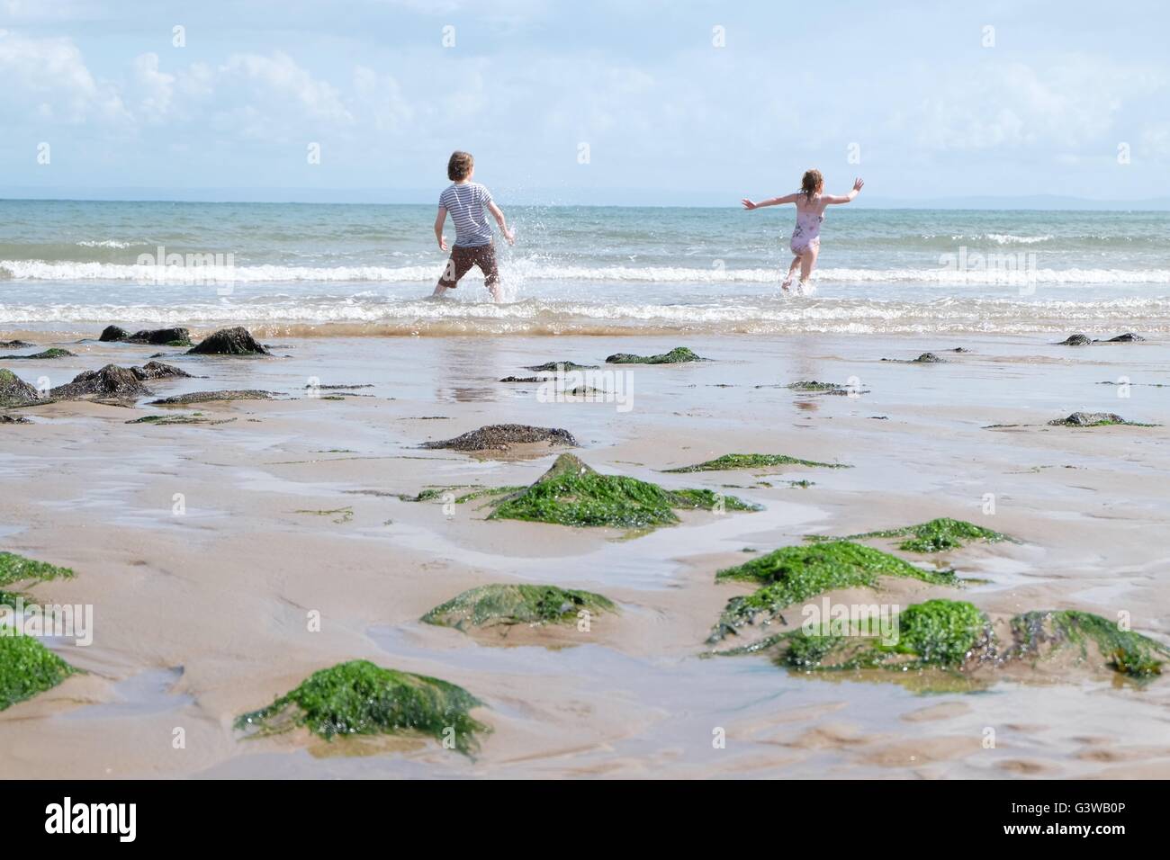 Ragazzo e ragazza in esecuzione a ondulazioni su una spiaggia con alghe marine in primo piano Foto Stock