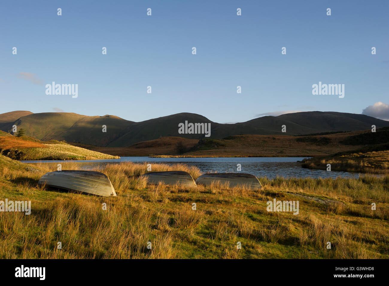 Tre barche rovesciata accanto al lago di sunrise in La montagne del Galles con crystal clear blue sky Foto Stock