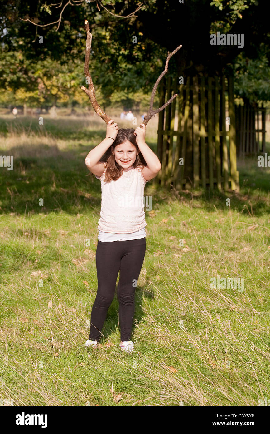 Riproduzione di fingere. Una giovane ragazza è larking intorno in un parco, giocare con alcuni rami morti fingendo sono palchi. Foto Stock