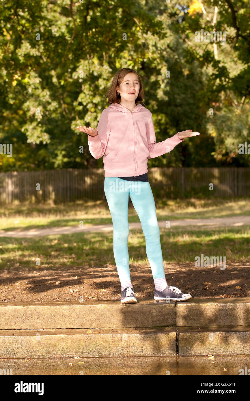 L'uno o l'altro. Una giovane ragazza sta sotto un albero sul bordo di una banca in calcestruzzo di un torrente, cercando di prendere una decisione. Foto Stock