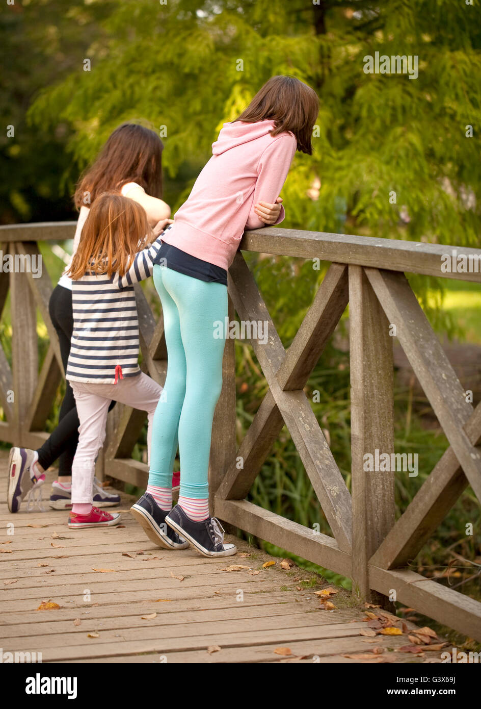 In piedi sul Tippy dita. Una giovane ragazza è in piedi sul suo tippy toes to peer oltre la ringhiera su un ponte a guardare le anatre al di sotto di Foto Stock
