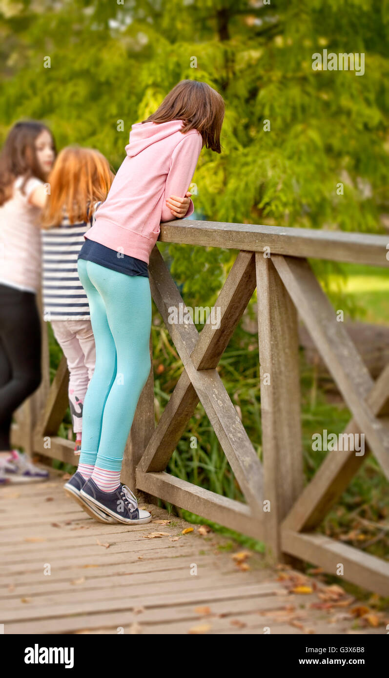 In piedi sul Tippy dita. Una giovane ragazza è in piedi sul suo tippy toes to peer oltre la ringhiera su un ponte a guardare le anatre al di sotto di Foto Stock